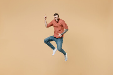 Fototapeta na wymiar Full size body length overjoyed happy tatooed young brunet man 20s short haircut open mouth wears apricot shirt jump show playing guitar gesture isolated on pastel orange background studio portrait