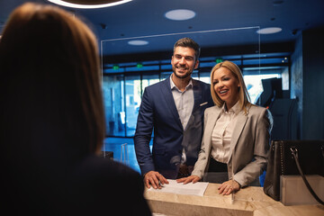 A smiling business couple with positive vibes and energy standing at the hotel reception and...