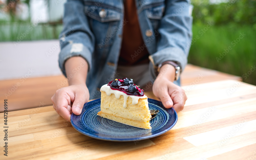 Wall mural Closeup image of a woman holding and serving a plate of blueberry cheesecake