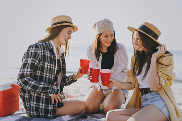 Full body three friend young women in straw hat summer clothes have picnic hang out together drink liguor holding glasses raise toasts outdoors on sea beach background People vacation journey concept
