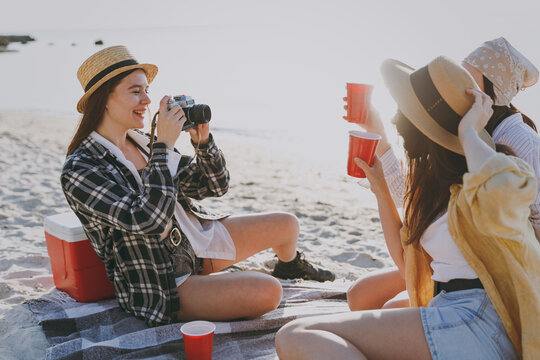 Three friends young women 20s in straw hat summer clothes have picnic hang out take photo together drink liguor have fun raise toasts outdoors on sea beach background People vacation journey concept