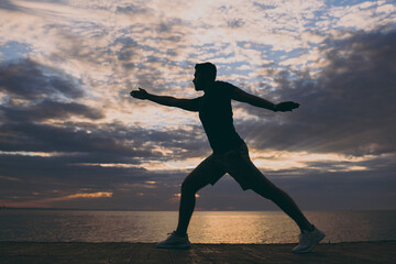 Fototapeta na wymiar Full size side view young strong sporty athletic fit sportsman man in sports clothes warm up training do lunges yoga asana at sunrise sun over sea beach outdoor on pier seaside in summer day morning