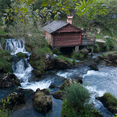 Small traditional wooden water mill by the wild river Krupa with big rocks and cascades on popular...