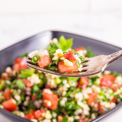 Ready-made tabbouleh salad in a bowl and on a fork, close-up