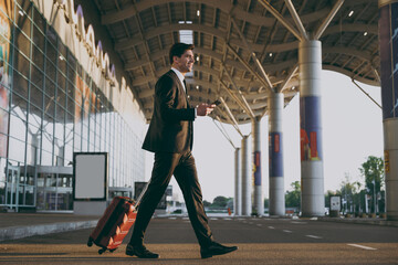 Bottom view full body young traveler businessman man in black suit walk outside at international airport terminal with suitcase use mobile cell phone book taxi order hotel Air flight business concept