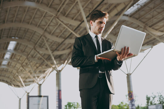 Bottom Side View Serious Young Traveler Businessman Man Wear Black Dinner Suit Walk Go Outside At International Airport Terminal Work Online On Laptop Pc Computer Air Flight Business Trip Concept.