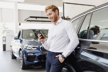 Man happy customer male buyer client wear white shirt talk mobile cell phone leaning on car choose auto want buy new automobile in showroom vehicle dealership store motor show indoor Sales concept