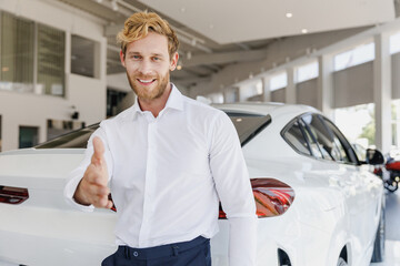 Fun man customer buyer client in white shirt stretch hand for shaking stand near car choose auto want buy new automobile in showroom vehicle salon dealership store motor show indoor. Sales concept.