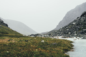 Atmospheric landscape with mountain creek among moraines in rainy weather. Bleak scenery with milky...