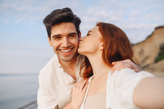 Close up smiling fun young couple two family man woman in casual clothes hug each other do selfie shot pov on mobile phone kiss at sunrise over sea beach outdoor seaside in summer day sunset evening