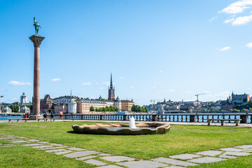 Amazing panorama of the capital of Sweden on a summer day. Small round fountain near Stockholm City Hall building. Ancient architecture. High Column with decorative sculpture on the top.
