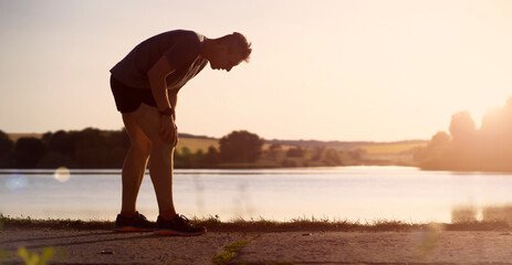 A young man jogging at sunset by the lake.