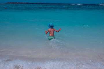 Cute joyful boy in swimming goggles standing up to the waist in water of the ocean