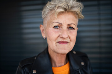 Portrait of senior woman standing against black backround, looking at camera.