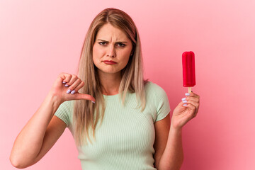 Young russian woman holding an ice cream isolated on pink background showing a dislike gesture, thumbs down. Disagreement concept.