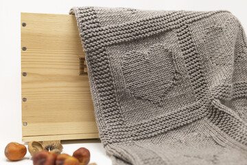 Light brown knitted blanket in Hearts pattern in wooden box on white background