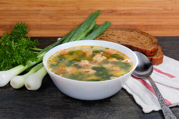 Bowl of clear salmon soup, greens, bread, spoon on napkin