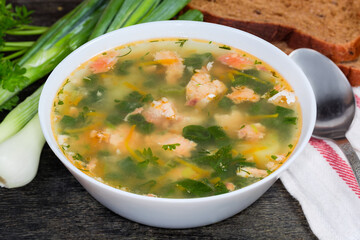 Bowl of clear salmon soup on dark surface, close-up