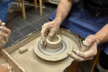 Hands of a man who learns to work with clay on potter's wheel