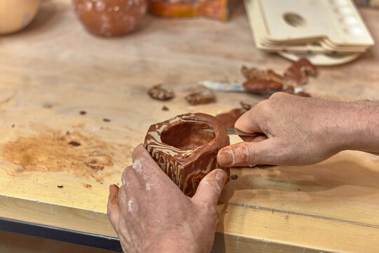 Hands of a ceramist who cuts a cup made in Japanese technique Nerikomi from red and light clay to develop the pattern