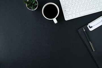 Black leather office desk table. Workspace with computer white keyboard and blank notebook, pen with equipment other office supplies. Top view with copy space, flat lay.