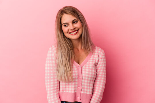 Young russian woman isolated on pink background looks aside smiling, cheerful and pleasant.
