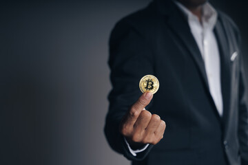 Naklejka na ściany i meble Handsome Investor Businessman in black suit holding a golden bitcoin on dark background, trading, Cryptocurrency, Digital virtual currency, alternative finance and investment Concept..