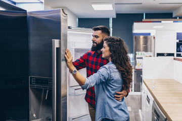 Young couple, satisfied customers choosing fridges in appliances store.