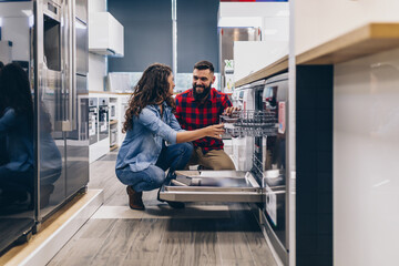 Beautiful and happy young couple buying dishwasher in modern appliances store.