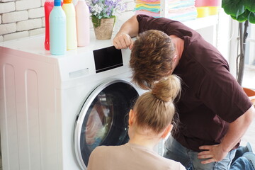 Caucasian couple looking at their washing machine broken at home while washing their clothes Couple...