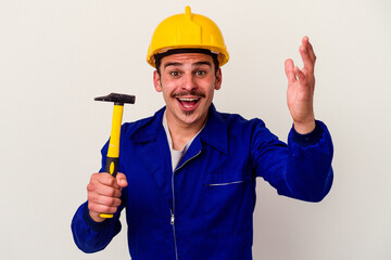 Young caucasian worker man holding a hammer isolated on white background receiving a pleasant surprise, excited and raising hands.