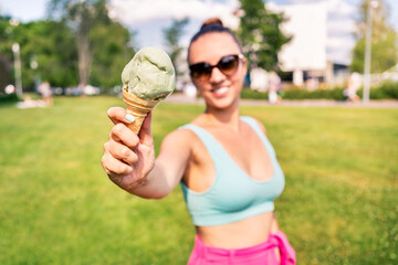 Fit slim woman showing ice cream cone in city park in summer. Happy smiling portrait of young...