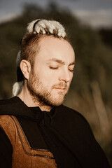 Close-up portrait of a young man with interesting depicts a Viking looks up thoughtfully with closed eyes.