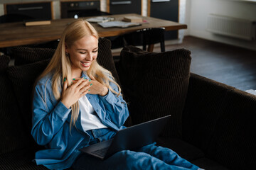 Happy woman sitting on sofa and using laptop