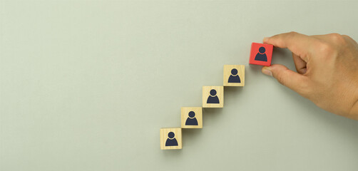Top view of human resources and recruiting business or team leader management concepts. Hand adult Asian man holding difference of people icon on  wooden block. Objects on grey paper background.