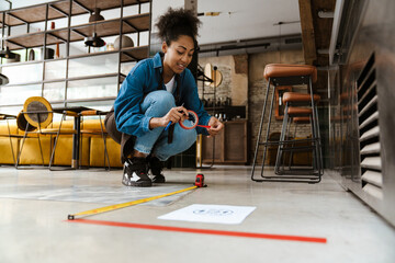 Obraz premium Black waitress in apron using tape measure while working at cafe