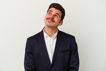 Young business caucasian man wearing wireless headphones isolated on white background dreaming of achieving goals and purposes