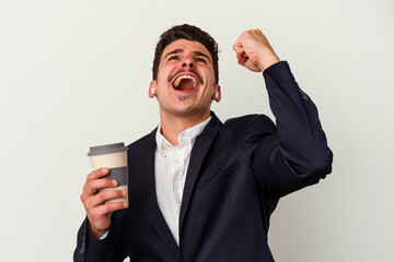 Young business caucasian man wearing wireless headphones and holding take way coffee isolated on white background raising fist after a victory, winner concept.