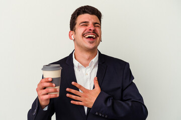 Young business caucasian man wearing wireless headphones and holding take way coffee isolated on white background laughs out loudly keeping hand on chest.