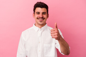 Young caucasian man isolated on pink background smiling and raising thumb up