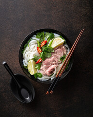 Pho Bo vietnamese soup with beef and rice noodles on a dark background, top view