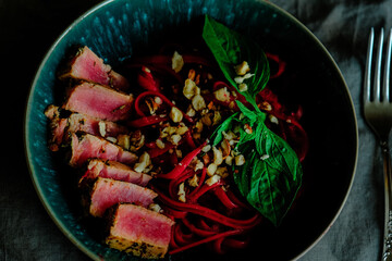 Tuna steak with linguine pasta, beetroot, hazelnut and ricotta sauce in blue bowl.