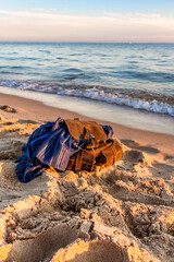Travel and vacation concept.   Empty sandy beach at sunset. Stylish brown backpack of traveler on...