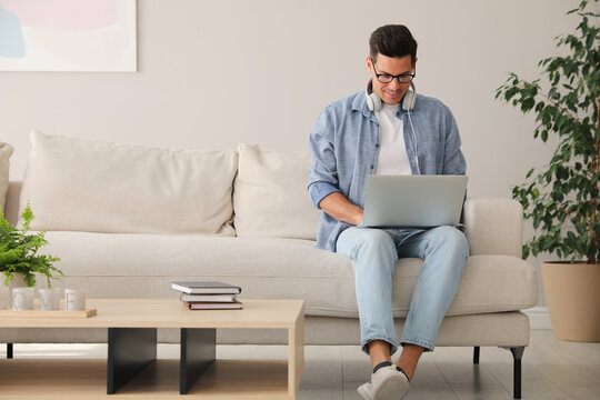 Man With Laptop And Headphones Sitting On Sofa At Home