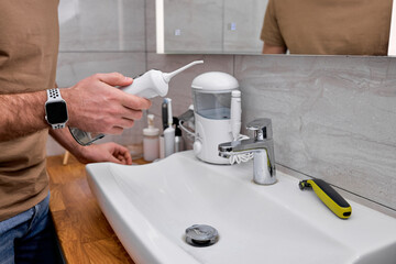 Cropped male casually dressed using oral dental irrigator with in bathroom near mirror. Young male begins the day with brushing cleaning teeth, side view portrait. copy space