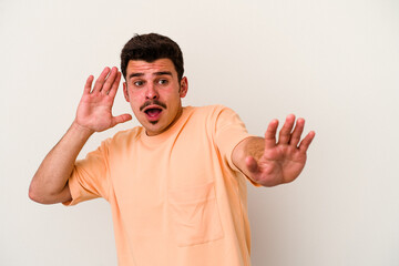 Young caucasian man isolated on white background being shocked due to an imminent danger
