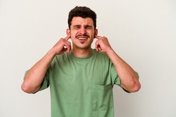 Young caucasian man isolated on white background covering ears with fingers, stressed and desperate by a loudly ambient.