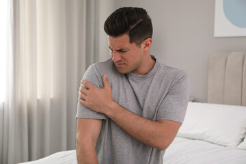 Man suffering from shoulder pain on bed at home
