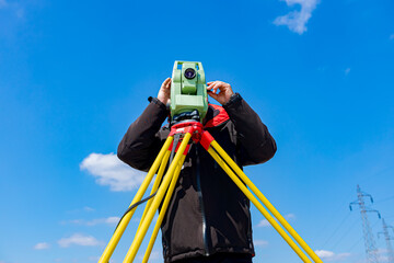Civil engineer, geodesist is working with total station on a building site, blue sky in background