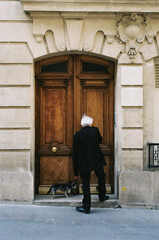 Snap of an old man going back home after walking his small dog out. He is just about to get in his parisian apartment.